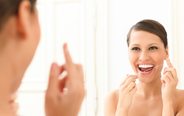 A young woman flossing her teeth in front of a mirror