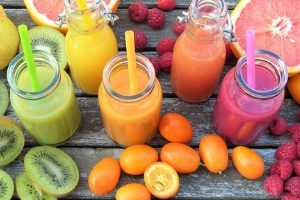A colourful arrangement of five glasses of fruit smoothie and fresh fruit