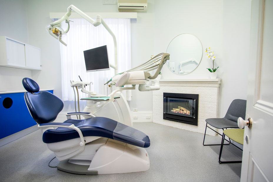 Treatment room for dental services, featuring a dark blue dental chair, quality fixtures and beautiful decor.