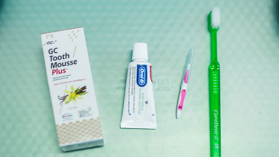 A pale green tray cover set up with items used for preventive dentistry, including Tooth Mousse, Toothpaste, interdental cleaner and green toothbrush.