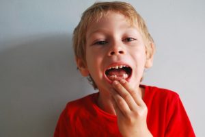 A young boy in red t-shirt showing that his two lower front teeth are missing
