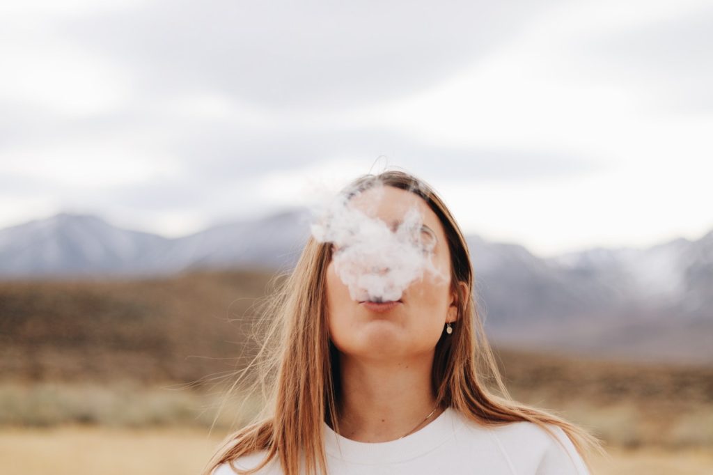 Young woman exhales a cloud of cigarette smoke, obscuring her face